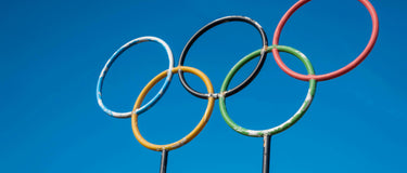 Five interlocking Olympic rings in blue, yellow, black, green, and red on a white background, symbolizing the unity of five continents