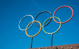 Five interlocking Olympic rings in blue, yellow, black, green, and red on a white background, symbolizing the unity of five continents